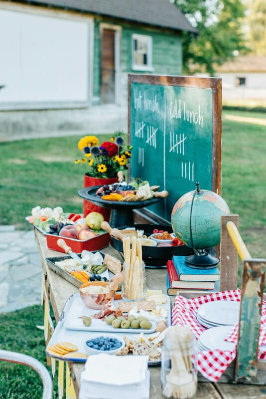 a picnic table with food on it in front of a green chalkboard and flowers