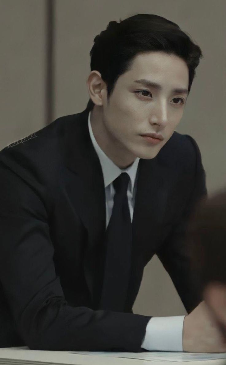 a man in a suit and tie sitting at a table with his hand on the desk