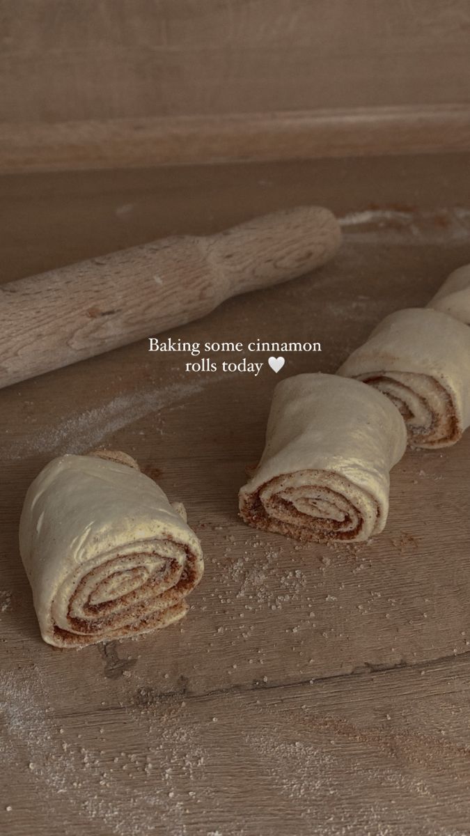 rolled up pastry sitting on top of a wooden table next to a rolling pin with the word baking some cinnamon rolls today