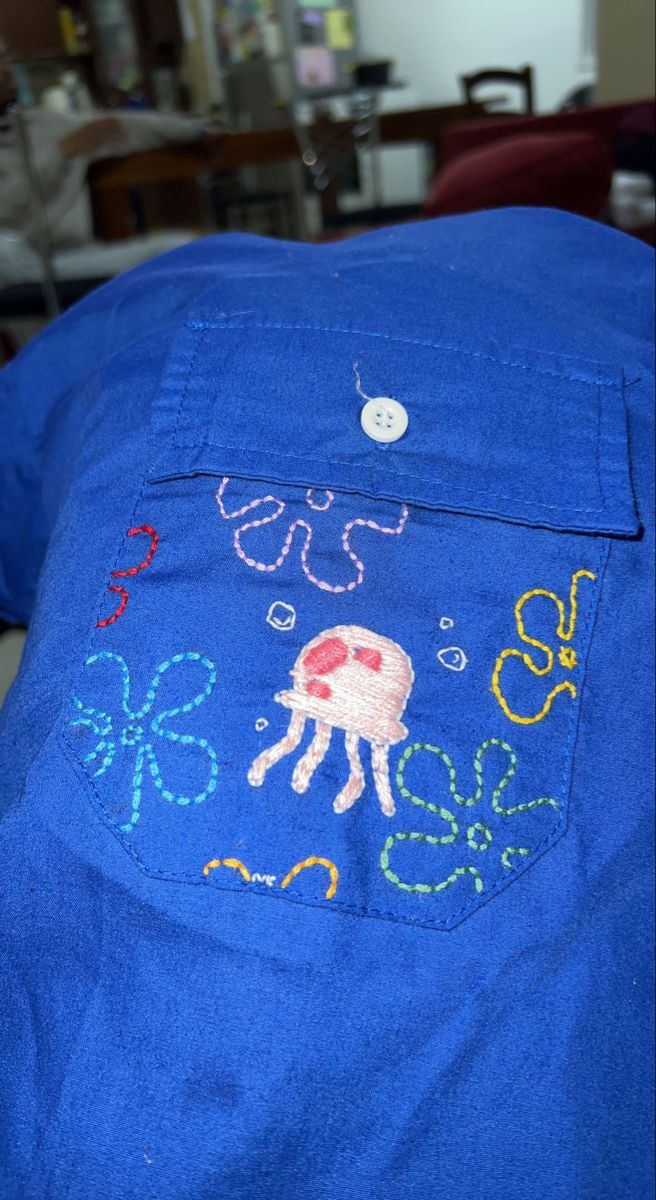 a blue shirt with an octopus embroidered on the front and back pocket, sitting on a table