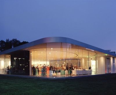 a group of people standing in front of a glass building at night with lights on