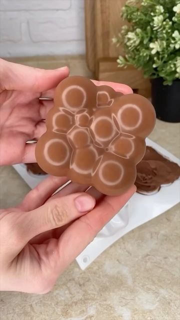 two hands holding a chocolate bar in front of a flower shaped box with hearts on it