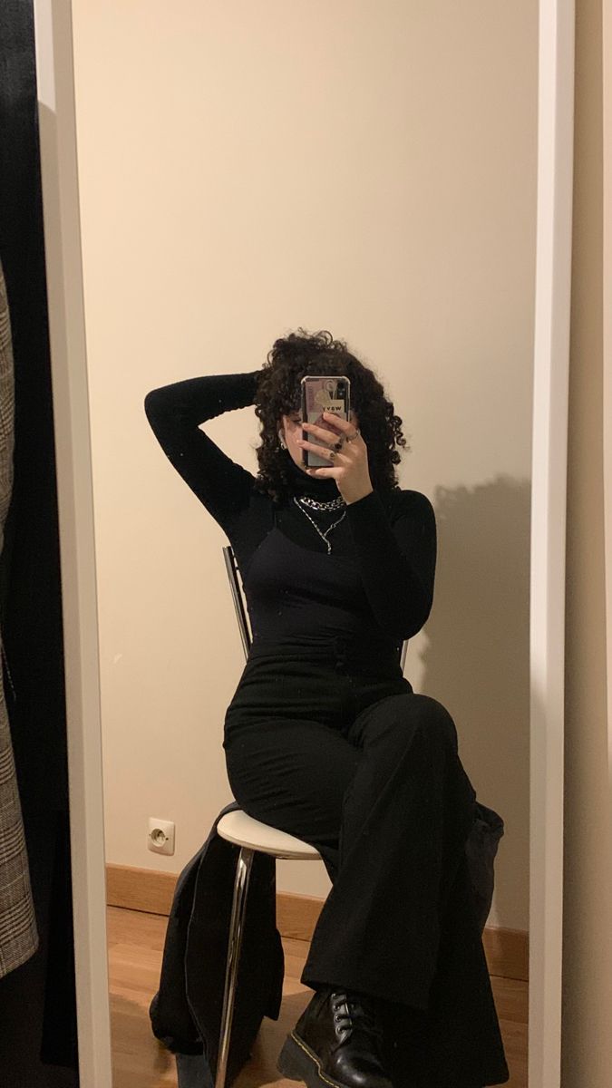 a woman sitting on a stool taking a selfie in the mirror with her cell phone