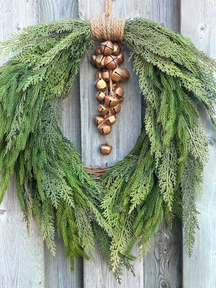 an evergreen wreath with acorns hangs on a wooden fence