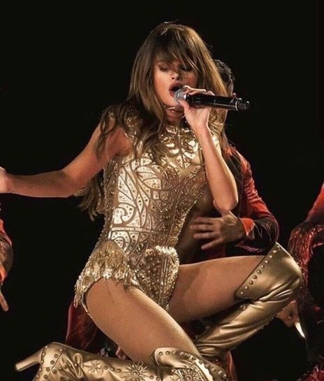 a woman in gold is performing on stage with her legs spread out and one leg up