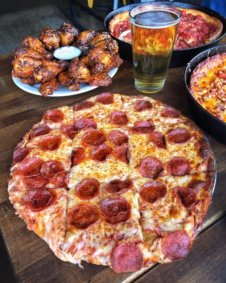 a pepperoni pizza sitting on top of a wooden table next to plates of food