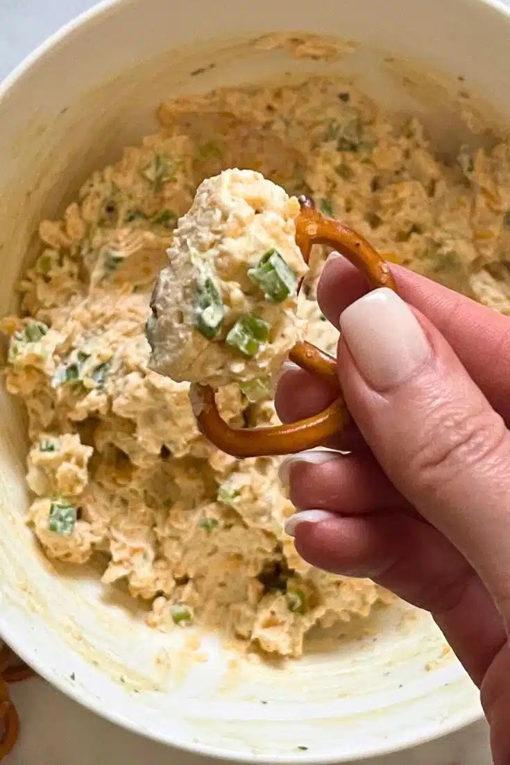 a hand holding a pretzel over a bowl of food