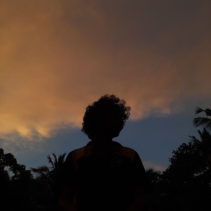 the silhouette of a person standing in front of a cloudy sky with trees behind them