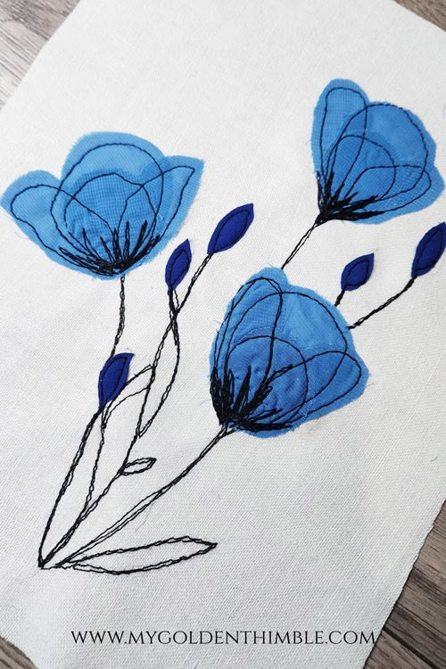 some blue flowers are on a white piece of cloth with black thread and stitching