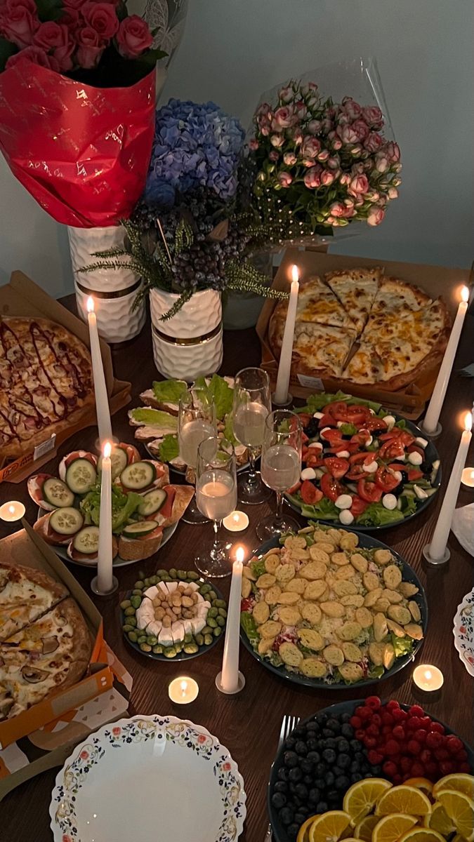 a table topped with lots of different types of food next to lit candles and flowers