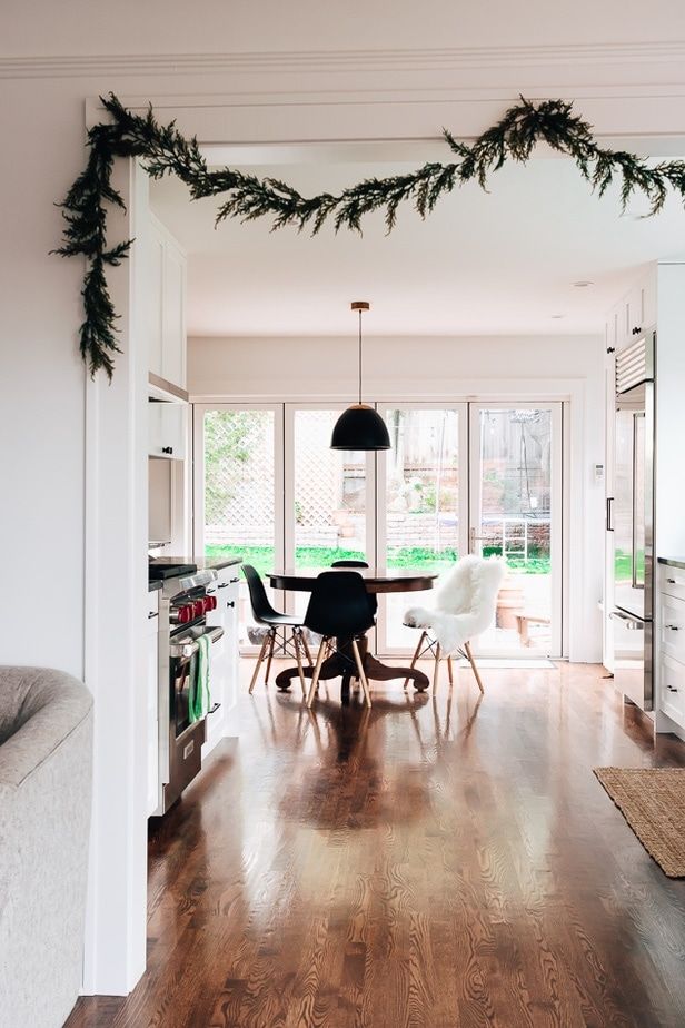 a dining room table and chairs in front of an open kitchen door with christmas garland hanging from the ceiling