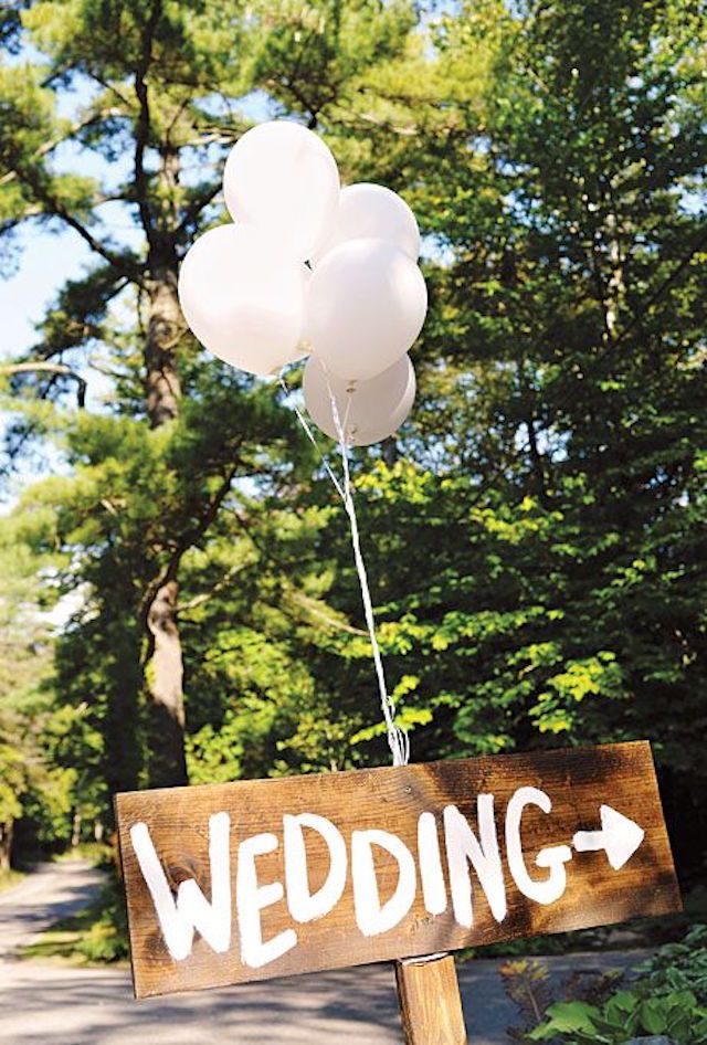 a wooden sign with balloons attached to it that says wedding and is in front of some trees