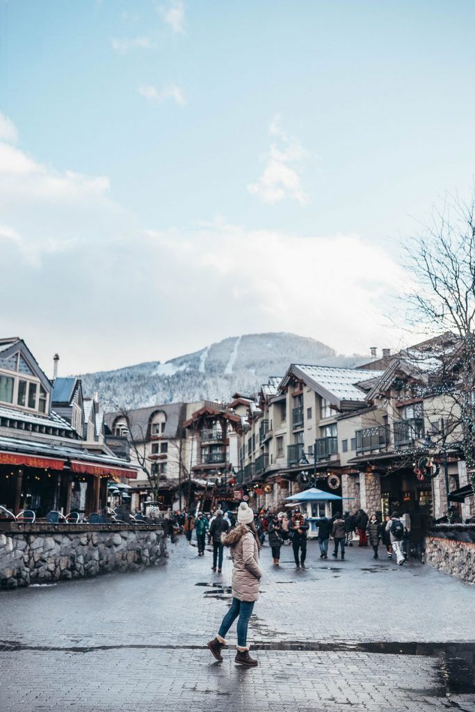 a woman walking down a street in front of buildings with mountains in the back ground