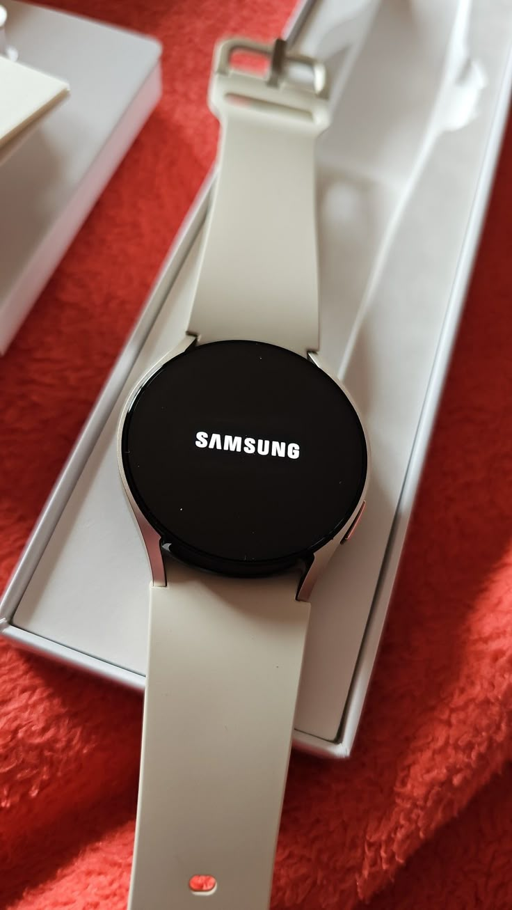 a samsung watch sitting on top of a white box next to a red cloth covered table