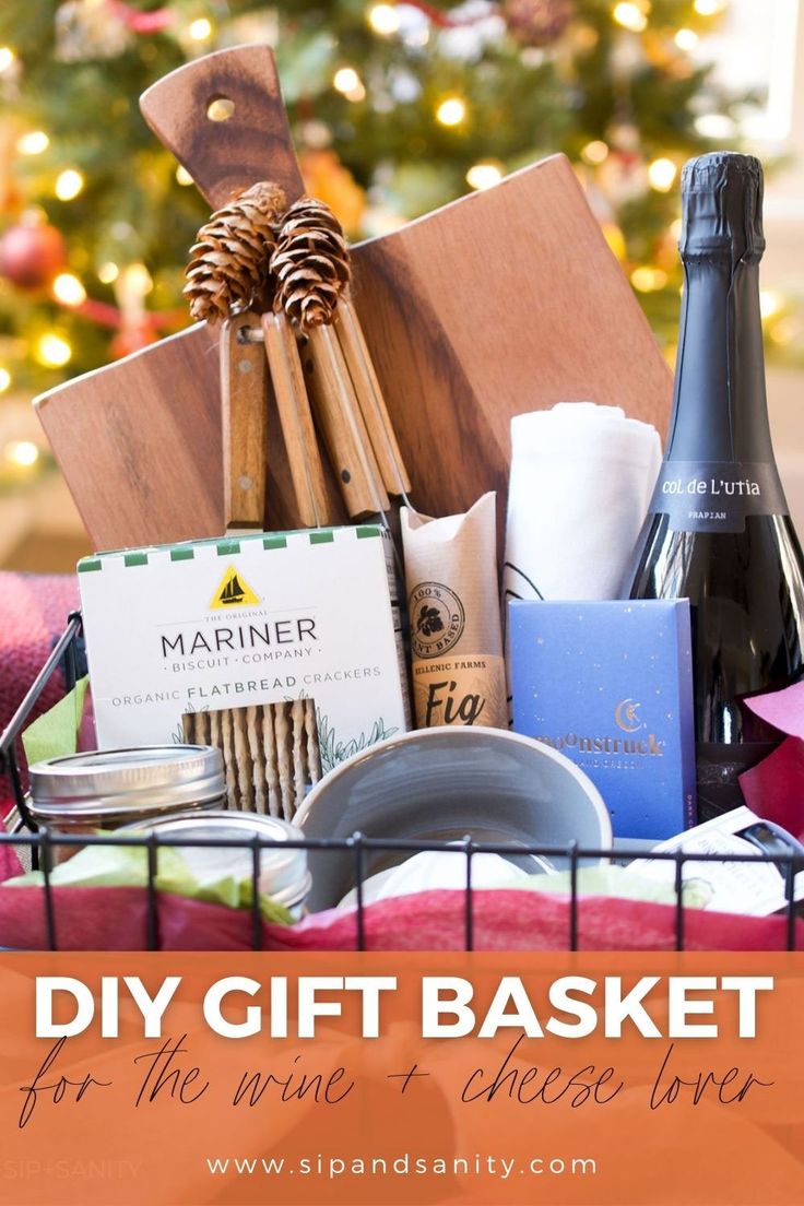 a basket filled with wine, cheese and other food items in front of a christmas tree