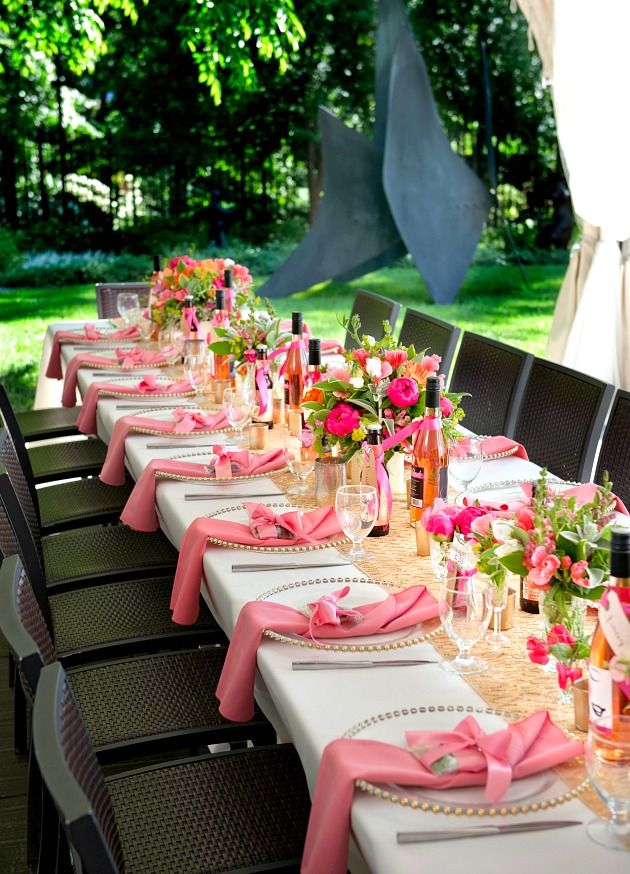 a long table is set with pink napkins and place settings for an outdoor event