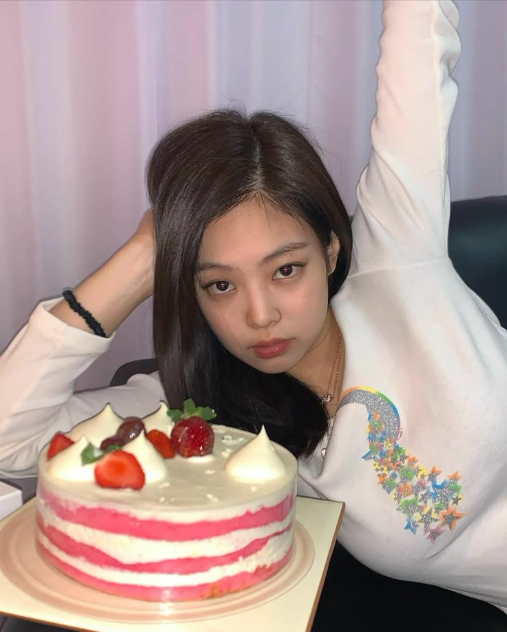 a woman sitting in front of a cake with strawberries on it and holding her arm up