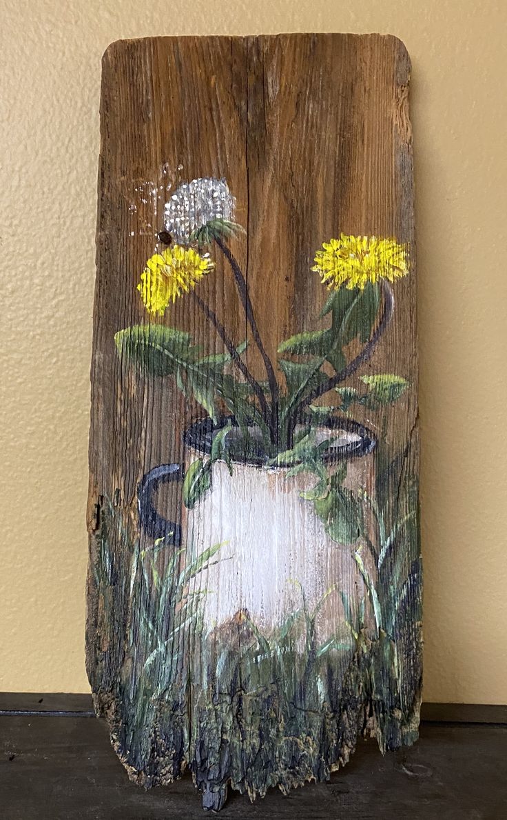 a wooden sign with flowers painted on it's side and grass growing out of the vase