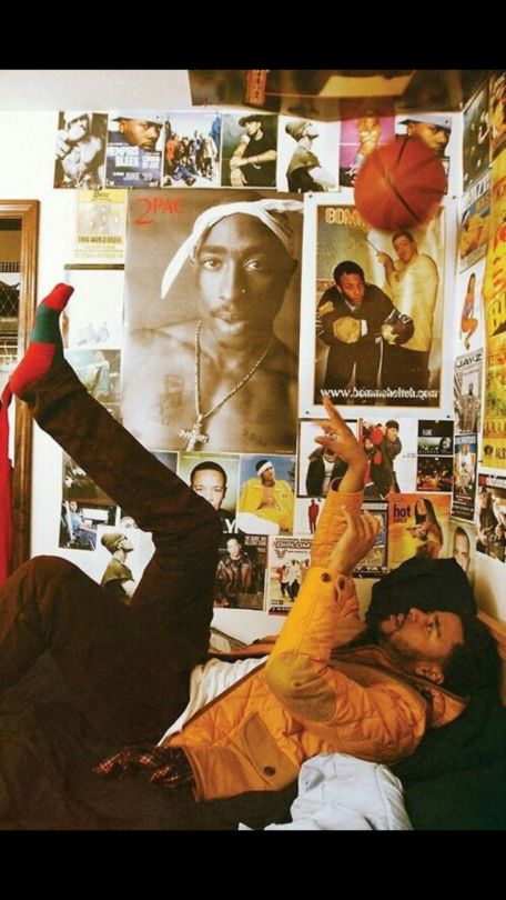 a man laying on top of a bed in front of a wall covered with posters