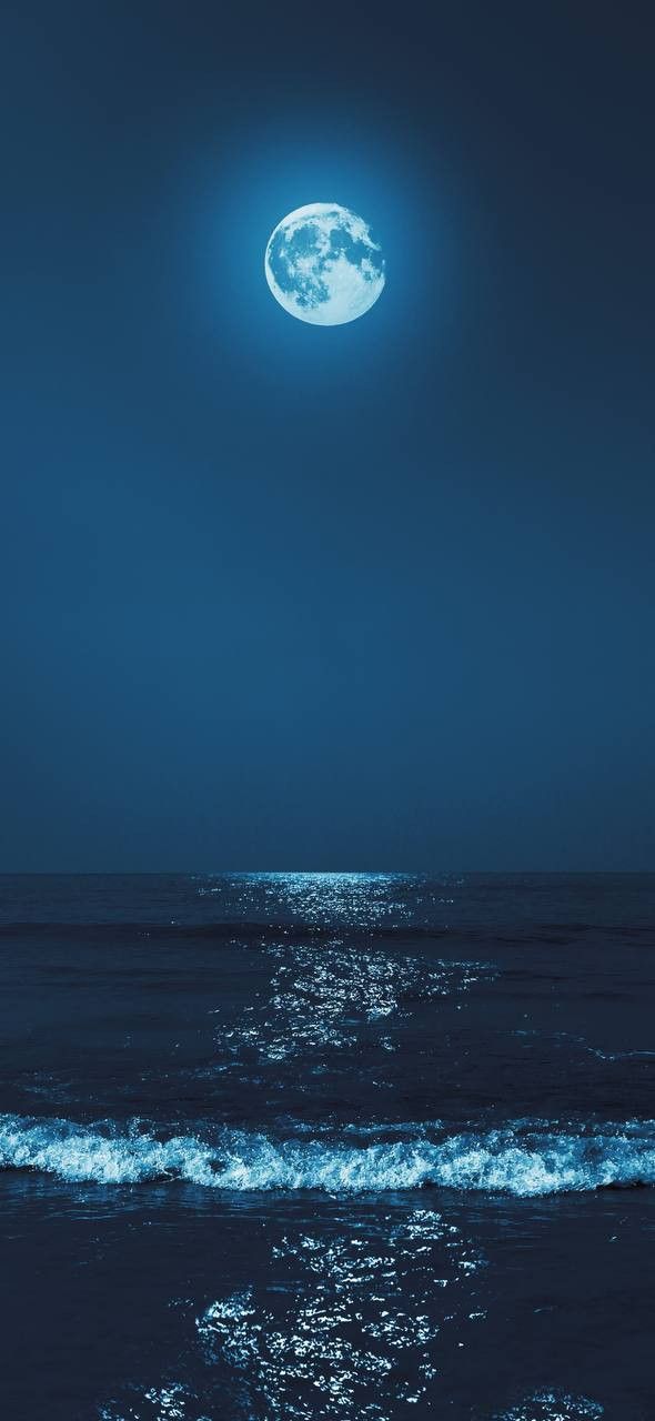 the moon is shining over the ocean with waves coming in to shore and blue sky