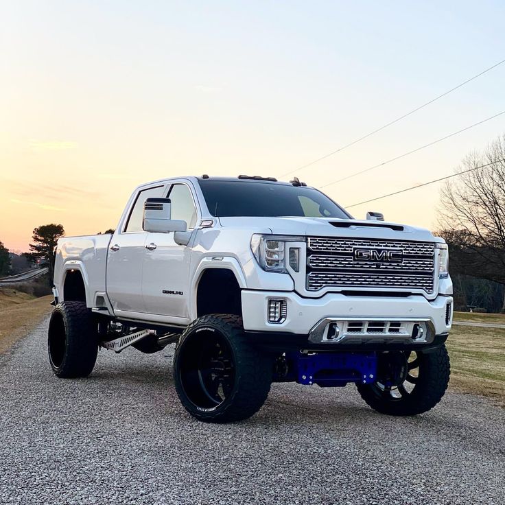 a large white truck parked on top of a gravel road in front of a field