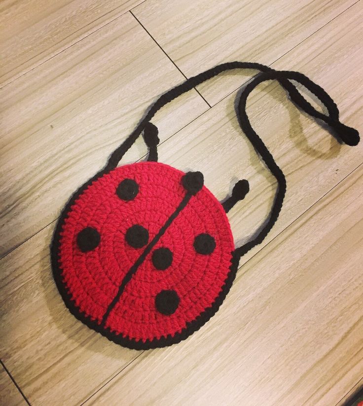 a crocheted red and black ladybug purse on the floor with a string