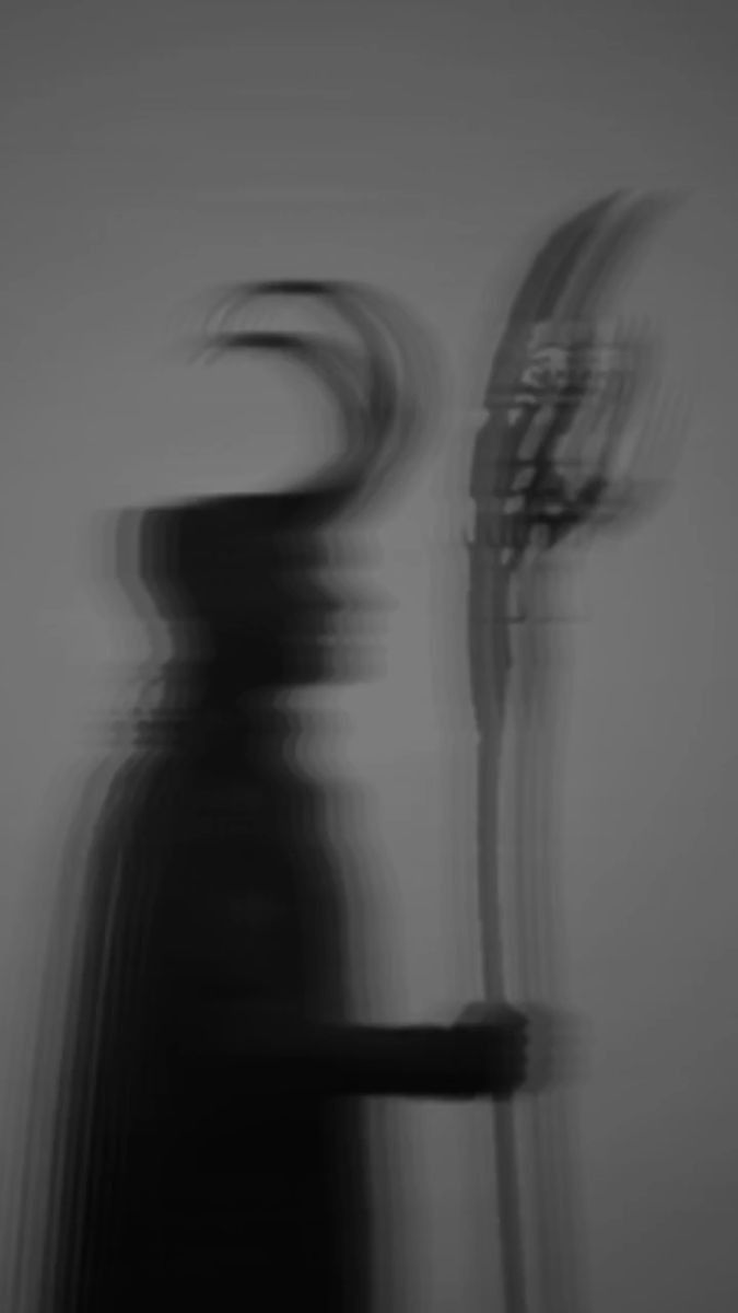 a black and white photo of a person with a hat on holding a wind chime