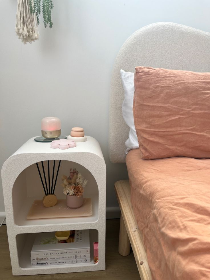 a bed with pink sheets and pillows next to a white night stand on the floor