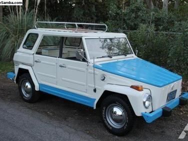 an old white and blue car parked on the side of the road with trees in the background