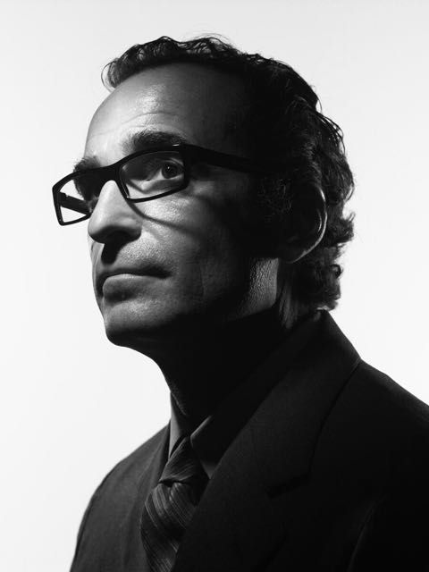 a black and white photo of a man with glasses looking off to the side wearing a suit