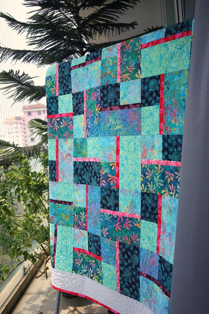 a blue and pink quilt hanging on the side of a wall next to a window