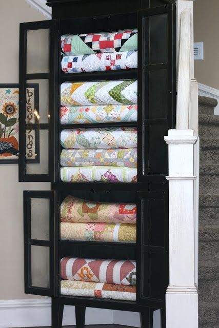 a black cabinet with many folded quilts on it's sides and stairs in the background