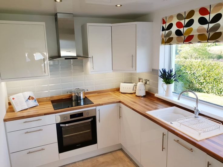 a kitchen with white cupboards and wooden counter tops next to a window that has a potted plant on it