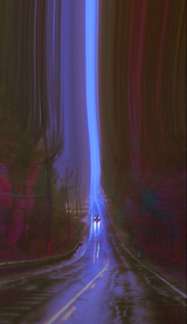 an empty road in the middle of a forest with blue and red lights on it