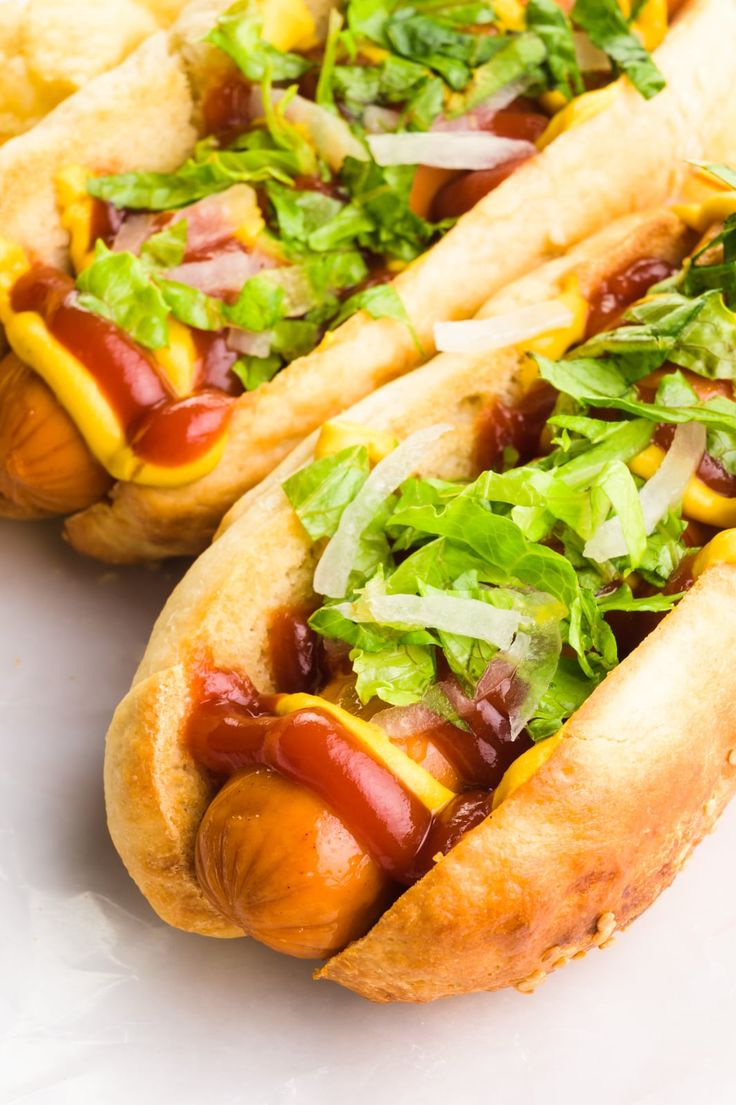 two hotdogs with ketchup, mustard and lettuce on them