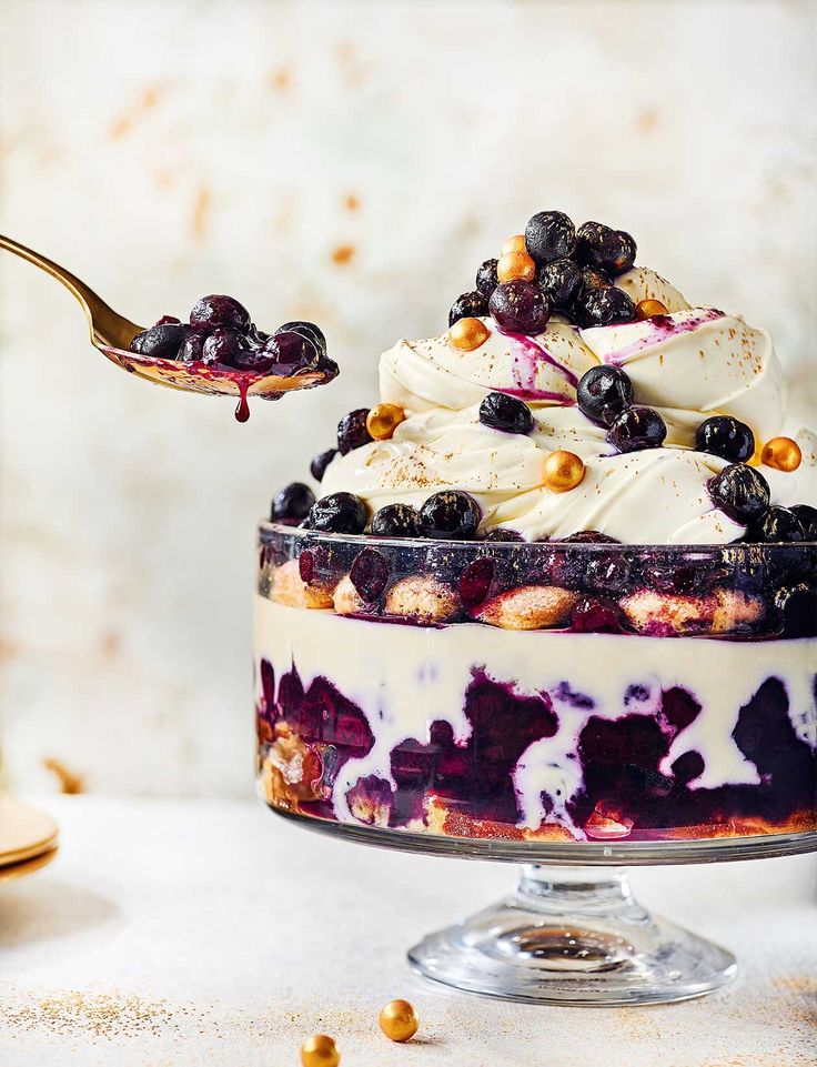 a dessert with blueberries and whipped cream is being spooned into the bowl by a fork