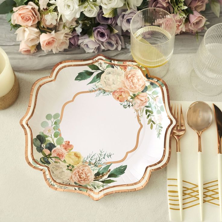 a table setting with floral plates and silverware, gold utensils and napkins