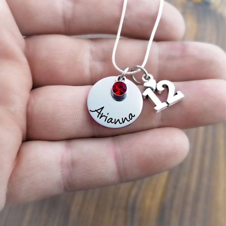 a person holding a necklace with the word avana written on it and a heart charm