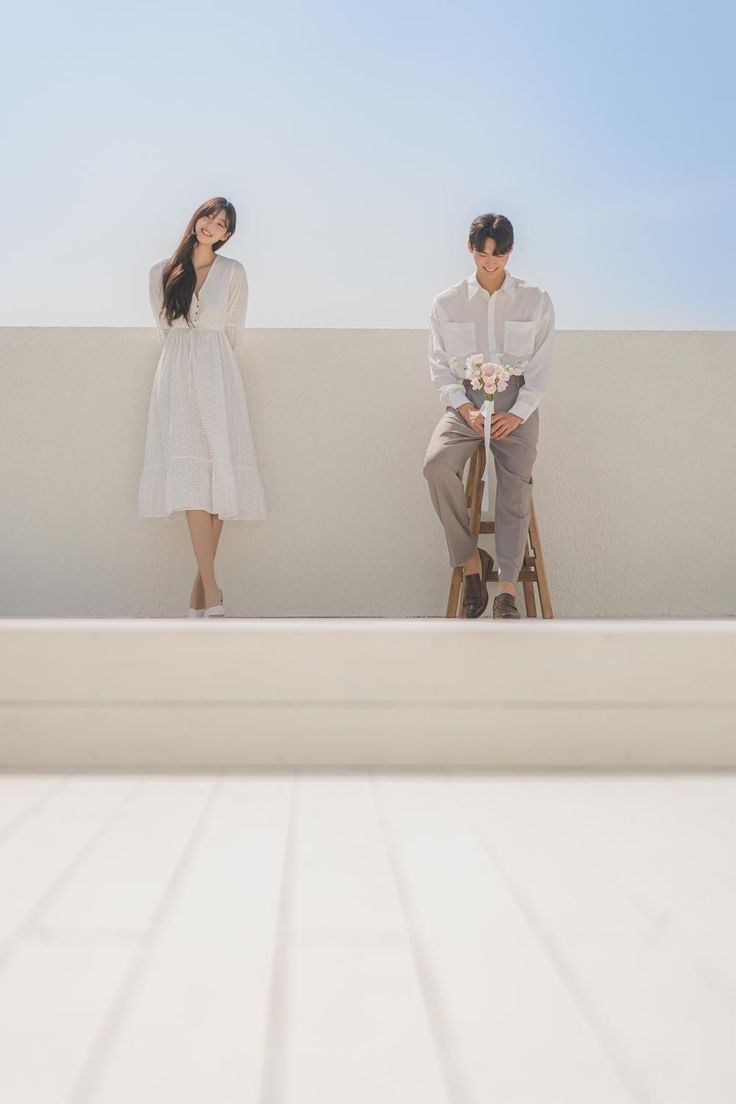 a man and woman sitting on top of a white wall next to each other with flowers in their hands