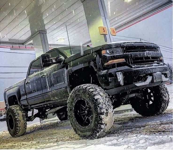 a black truck is parked in front of a building with snow on the ground and it's tires