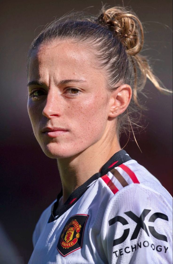 a female soccer player with a ponytail in her hair looking at the camera while wearing a jersey