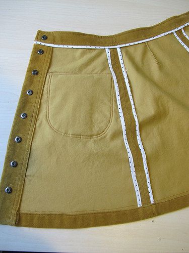 a yellow skirt with white trim and buttons on the side is sitting on a table