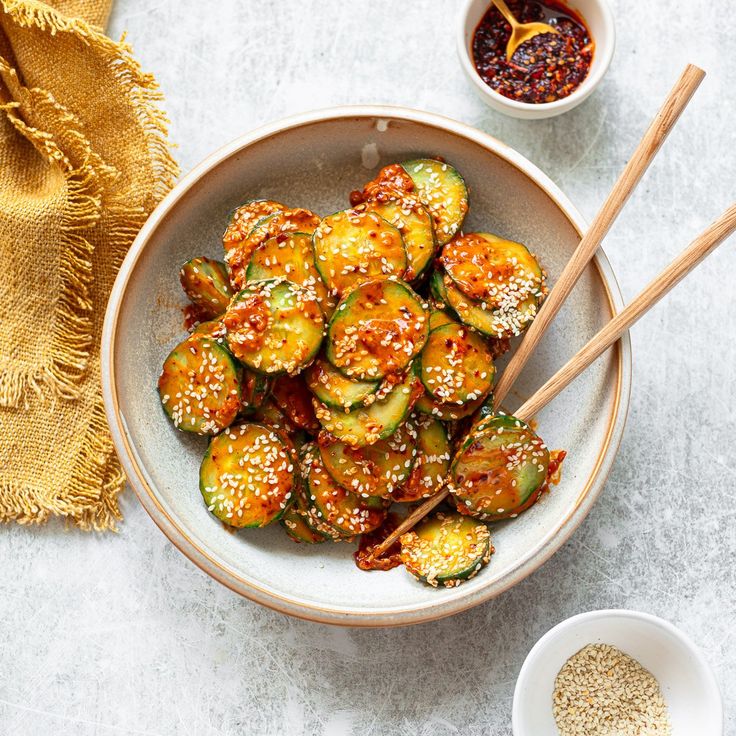 a bowl filled with zucchini and sesame seeds next to two bowls of seasoning