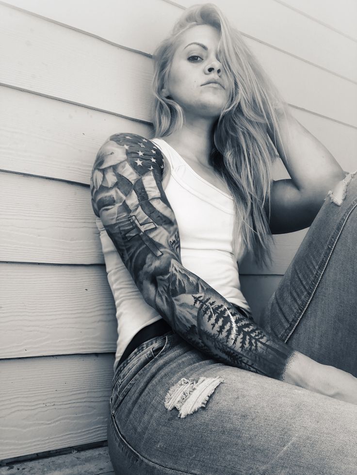 a woman sitting on the ground with her arms behind her head and tattoos on her arm