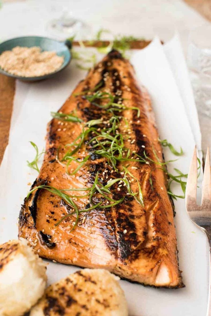 grilled salmon and potatoes on a white plate with fork and knife next to it