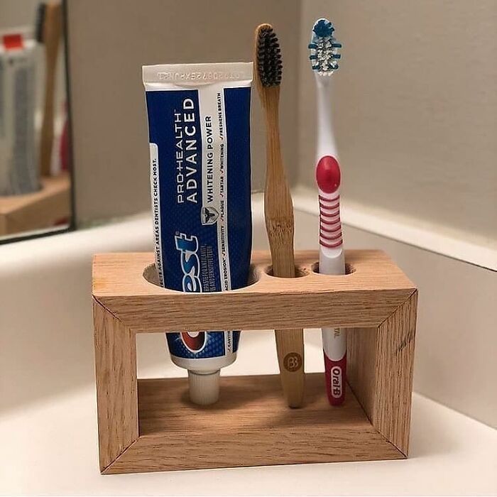 two toothbrushes and one tube of toothpaste are in a wooden holder