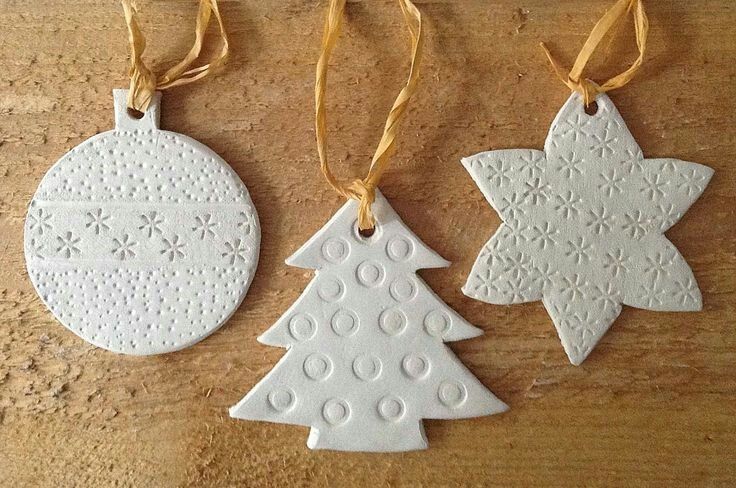 three white ceramic christmas ornaments hanging from twine on a wooden table with yellow ribbon