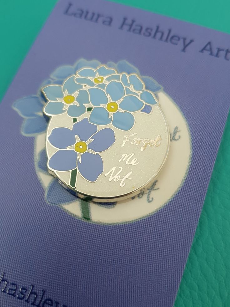 there is a blue and white flower on the back of a brooch that says forget me not