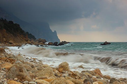 a rocky beach with waves crashing on the shore and rocks in the foreground, under a cloudy sky