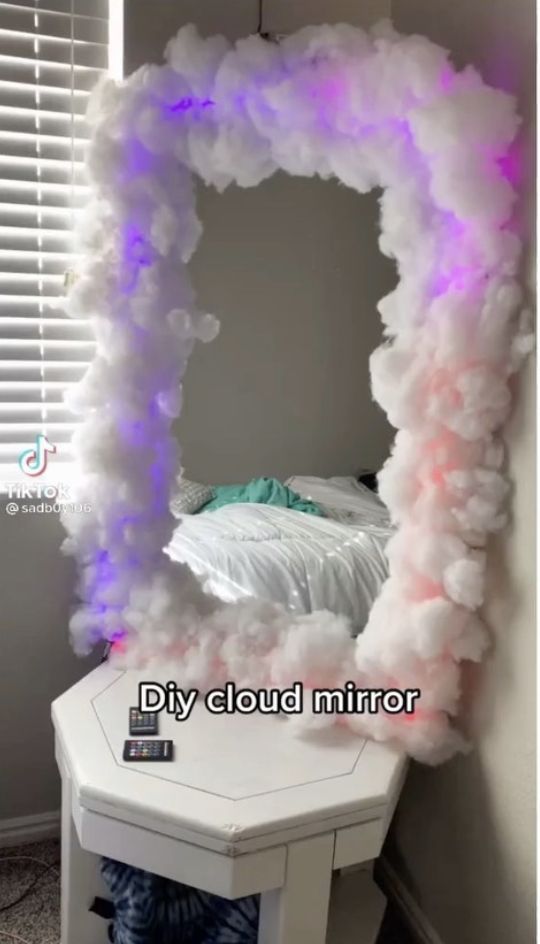 a white bed sitting under a purple light next to a mirror on top of a table